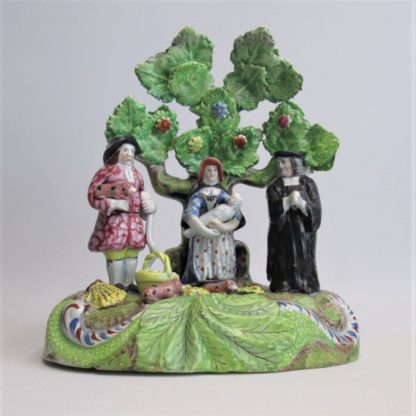 A Staffordshire pearlware 'Tythe Pig' group, depicting the farmer, holding a pig with other produce of bushels of corn and his wife holding a baby.   Circa 1820